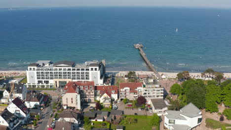 Aerial-view-flying-above-buildings-facing-Baltic-sea-beach-coastline-on-summertime-sunny-day,-Scharbeutz,-Germany,-sideways